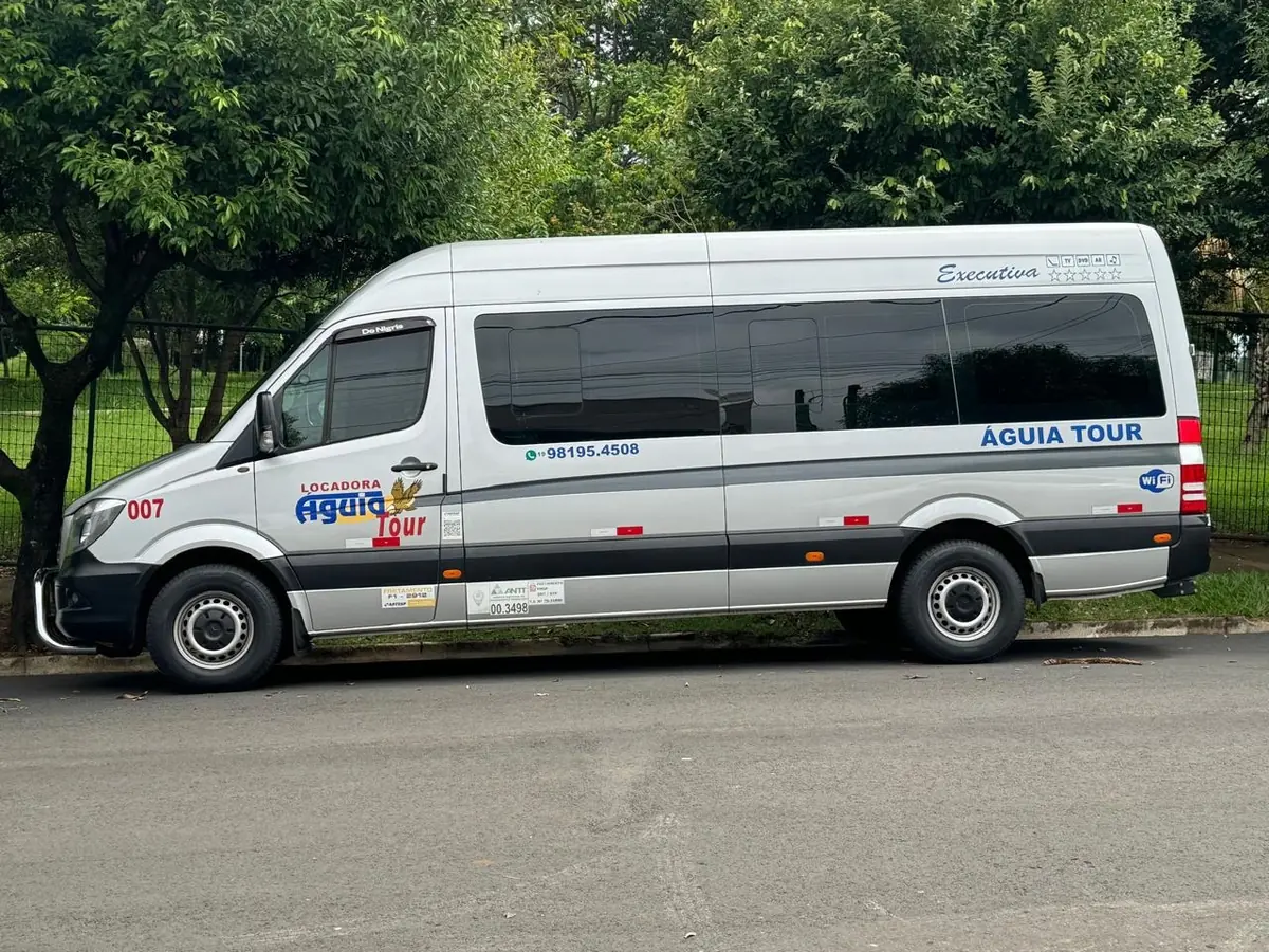 Van executiva da Águia Tour vista de lado em área arborizada